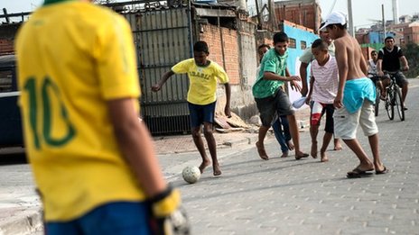 Boys playing street football on a paved road between brick walls