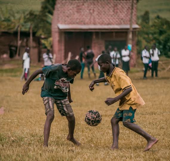Two boys playing with a football wound from twine outside a brick building
